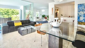 Een moderne woonkamer met een glazen eettafel, grijze banken en een groot raam met uitzicht op groen.