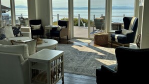 A spacious living room with a large view of the ocean, featuring a white sofa, a black armchair, and a wooden coffee table. - Oceanfront Luxury Retreat at Sandy Point Shores. (Ferndale)