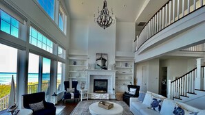 A spacious living room with a fireplace, large windows overlooking the ocean, and a balcony with a view of the sea. - Oceanfront Luxury Retreat at Sandy Point Shores. (Ferndale)