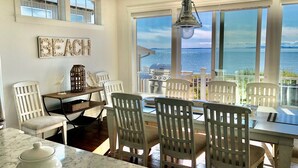 A dining area with a view of the sea, white chairs, a table, and a hanging light fixture. - Oceanfront Luxury Retreat at Sandy Point Shores. (Ferndale)