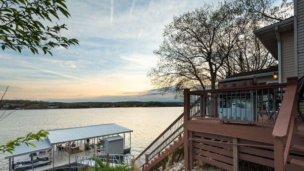 Une propriété située au bord de l’eau, dotée d’un quai, d’un espace salon couvert et d’une terrasse en bois offrant une vue sur un lac.