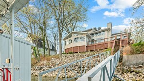 Une maison moderne dotée d’une terrasse en bois et d’un chemin de pierre menant à un quai.