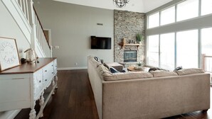 Un salon spacieux avec un grand canapé beige, un mur d’accent en pierre, une cheminée et un téléviseur fixé au-dessus.