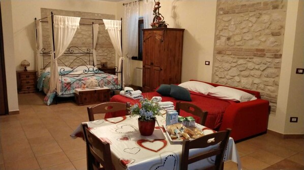 A bedroom with a double bed, a daybed, a wardrobe, a table with a vase, and a stone wall.