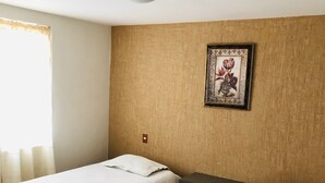 Ein Zimmer mit zwei Betten, einem Holzkopfteil, einem gerahmten Bild an der Wand und einem Fenster mit Vorhängen.