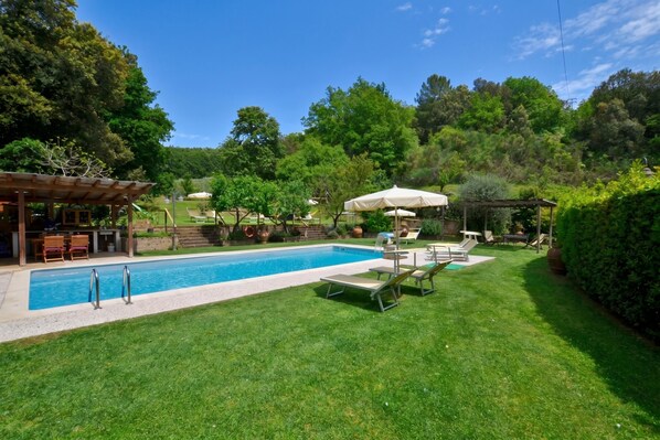 Ein Swimmingpool mit Liegestühlen und Sonnenschirmen, umgeben von einer gepflegten Rasenfläche und Bäumen.