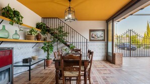 A dining area with a wooden table and chairs, a staircase with a railing, and a view of a car through a gate.