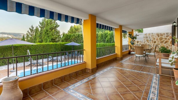 A covered patio with a pool, yellow walls, and outdoor furniture.