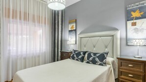 A neatly arranged bedroom with a bed, a bedside table, a lamp, and a wall with artwork.