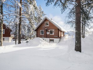 Une cabane en bois avec un toit en pente, entourée d’arbres couverts de neige et sous un ciel dégagé.