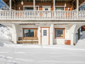 A wooden chalet with a balcony, a bench, and a door.