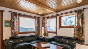 A room with a black leather sofa, a wooden coffee table, and a view of a snowy landscape through large windows.