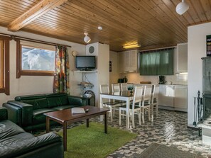 A cozy living area with a green sofa, a wooden coffee table, and a television. There's a dining table with chairs in the background.