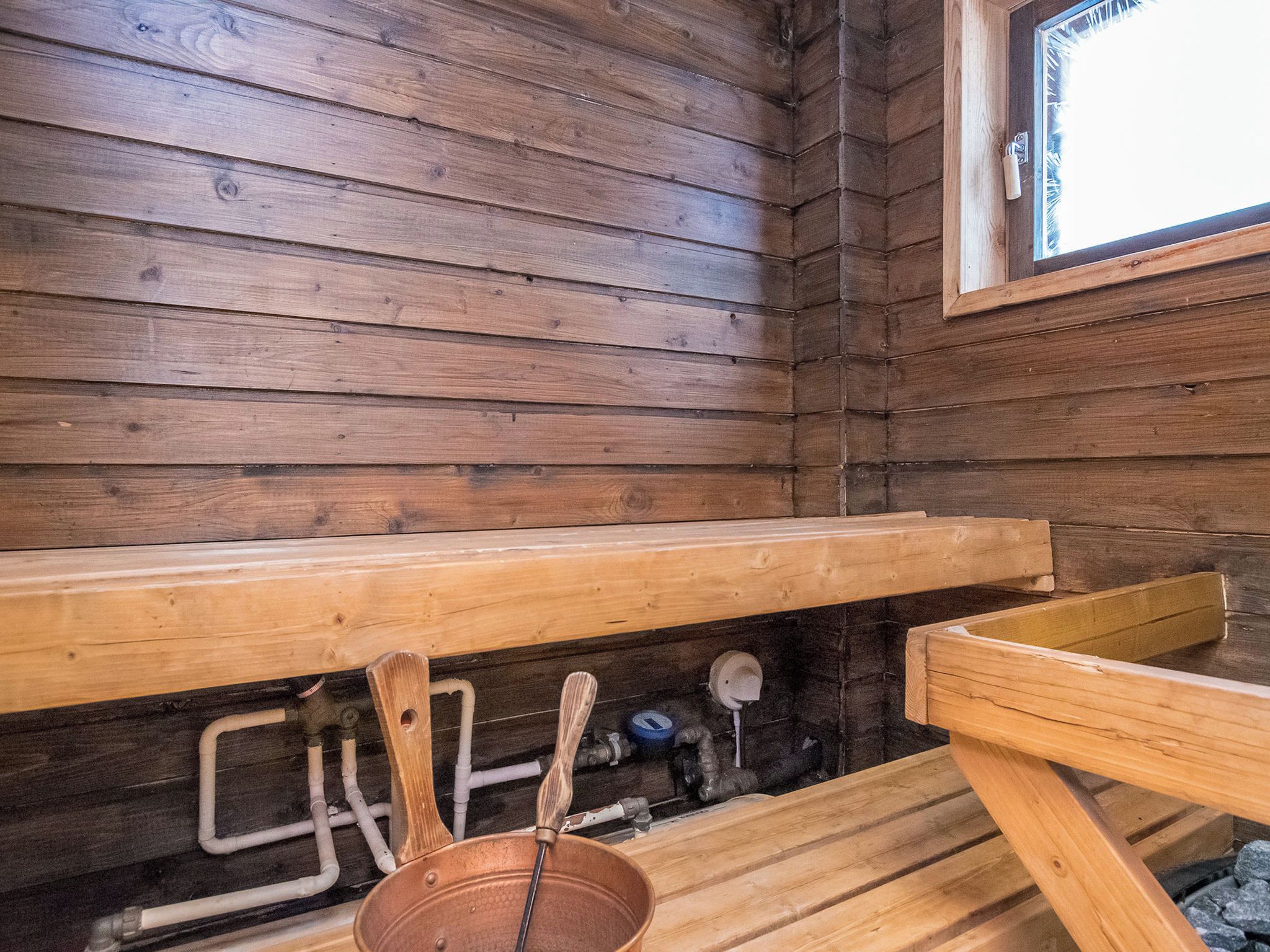A wooden cabin interior with a bench, a window, and visible plumbing.