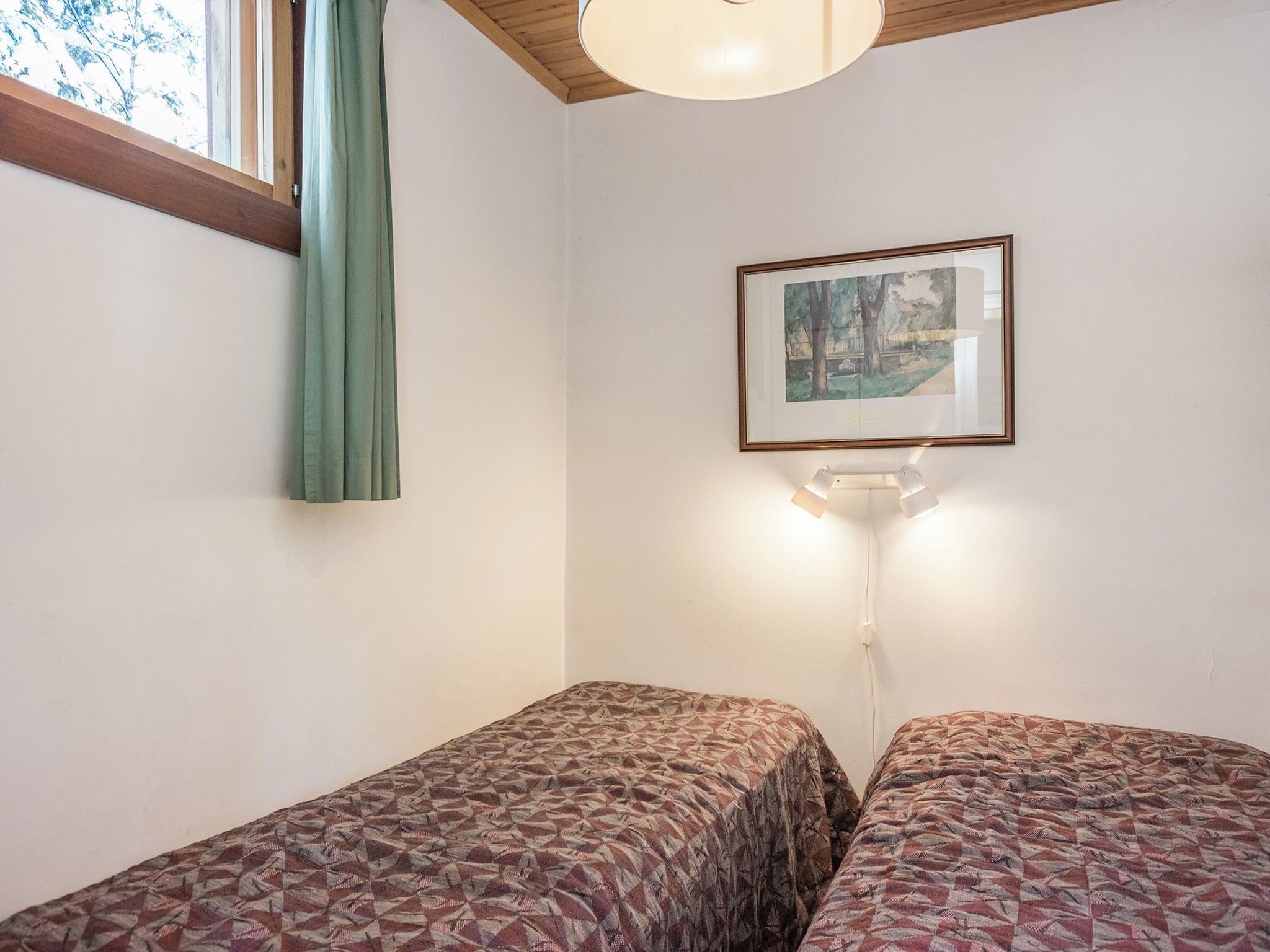 Una stanza con due letti singoli, un quadro appeso al muro, una finestra con tenda e una lampada a sospensione.