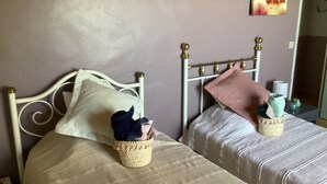 Ein Schlafzimmer mit zwei Betten, jeweils mit Kopfteil und Nachttisch. Über den Betten befindet sich eine Wanddekoration und auf der rechten Seite ein kleiner Tisch mit Vase und Kerze.