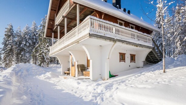 Un chalet de madera cubierto de nieve con un balcón, rodeado de árboles cargados de nieve.