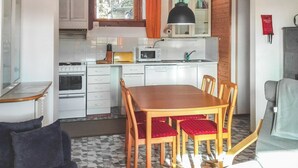 Una cocina compacta con armarios blancos, un microondas y un lavabo. Hay una mesa de comedor con cuatro sillas y una alfombra en el suelo.