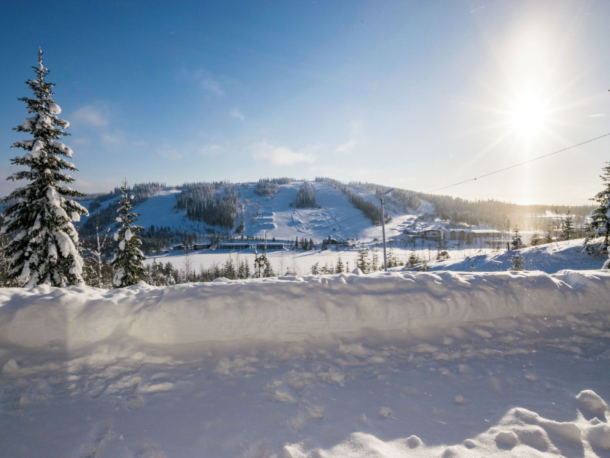 A snowy landscape with a ski slope, trees, and a clear sky.