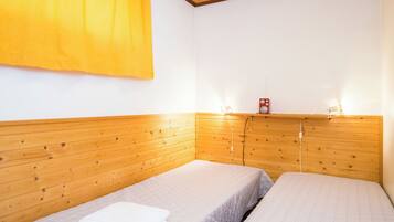 Une chambre avec deux lits, une tête de lit en bois, un rideau jaune et un haut-parleur rouge posé sur une étagère.