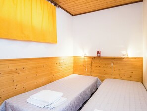 Een kamer met twee bedden, een houten hoofdeinde, een geel gordijn en een rode speaker op een plank.