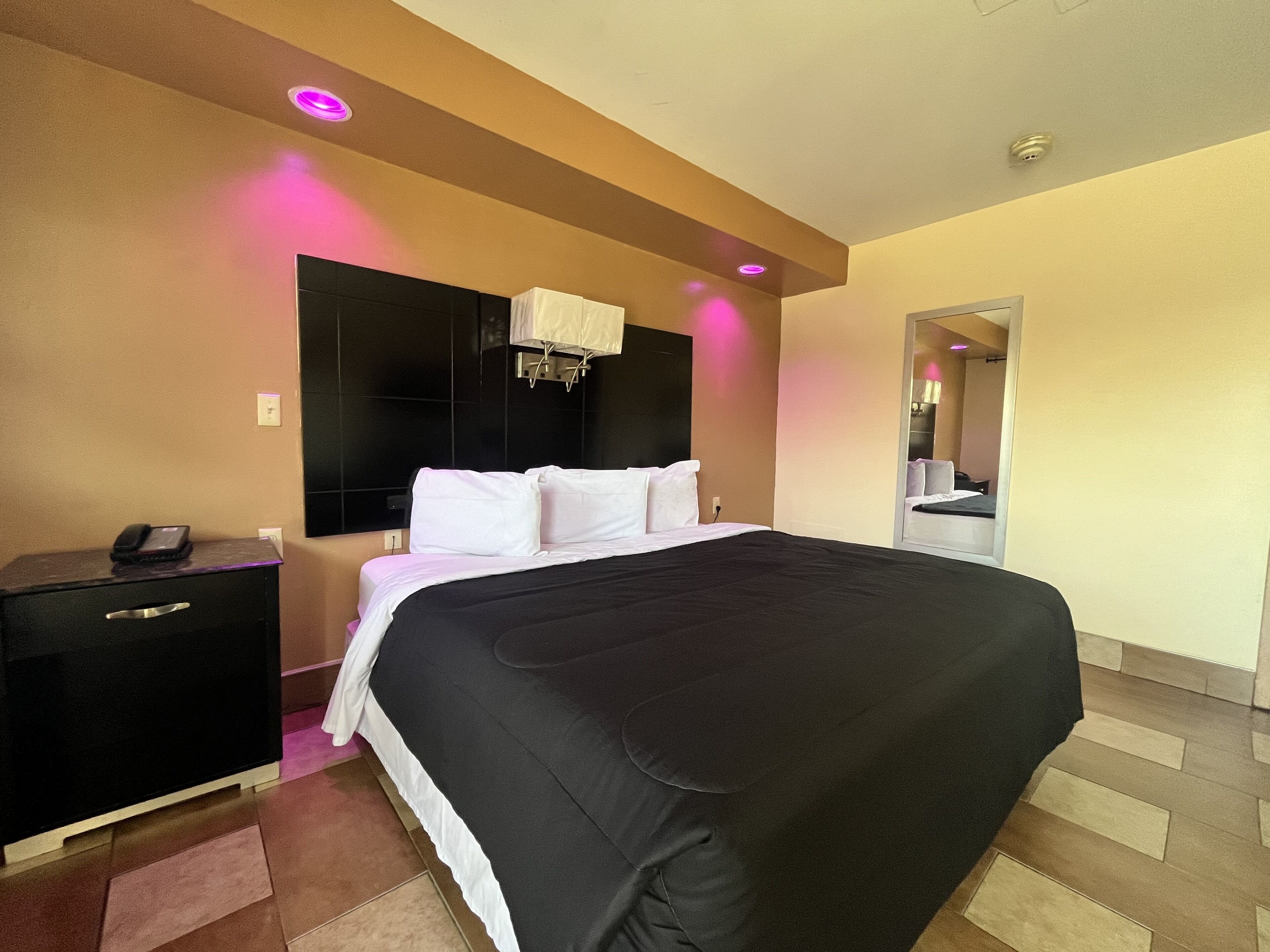 A modern hotel room with a large bed, a bedside table, a mirror, and a ceiling light.