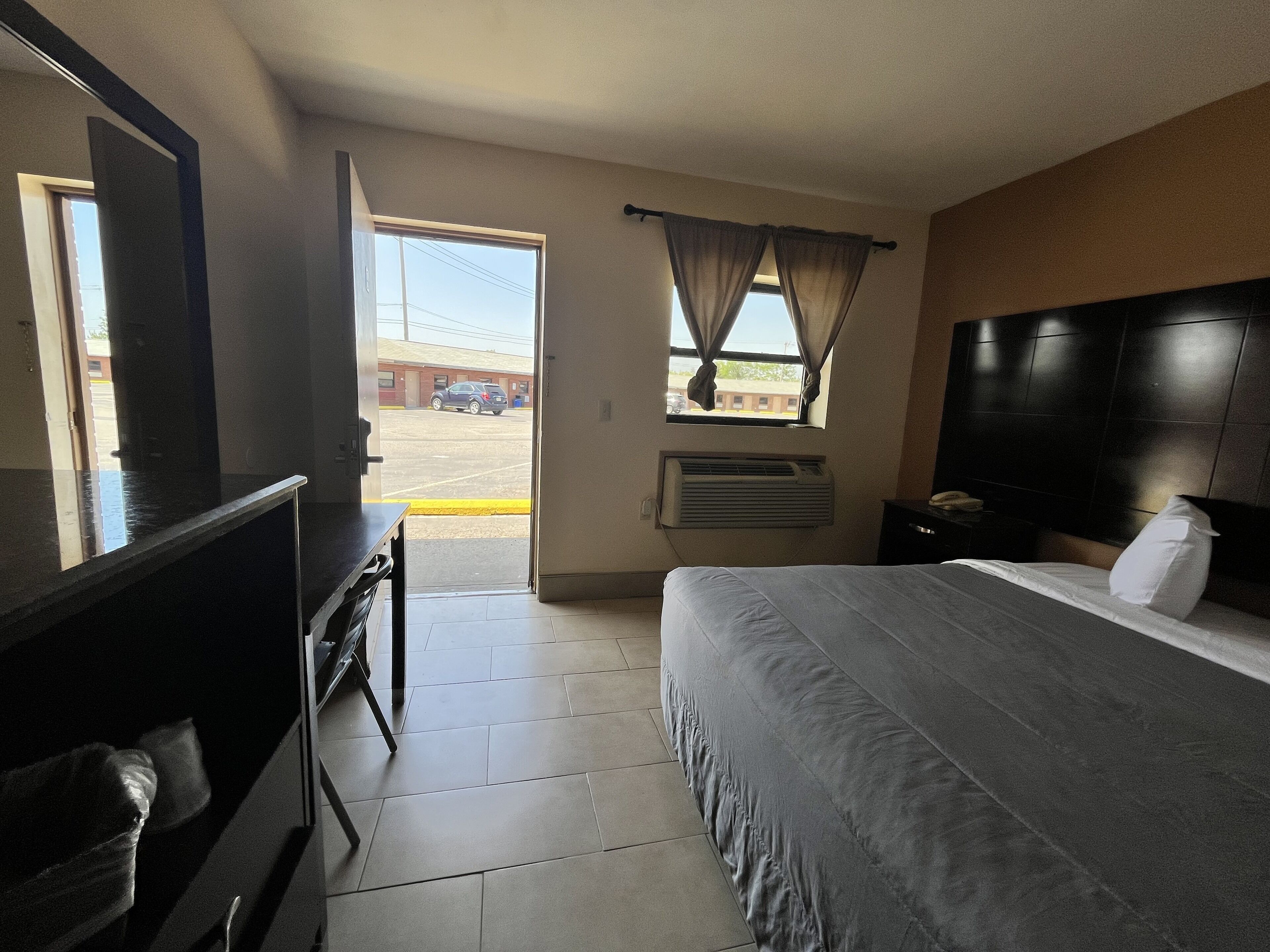 Une chambre d’hôtel équipée d’un lit, d’un bureau, d’une chaise, d’une fenêtre avec des rideaux et d’un appareil de climatisation.