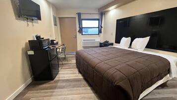 A hotel room with a bed, a desk with a computer, a TV, and a window.