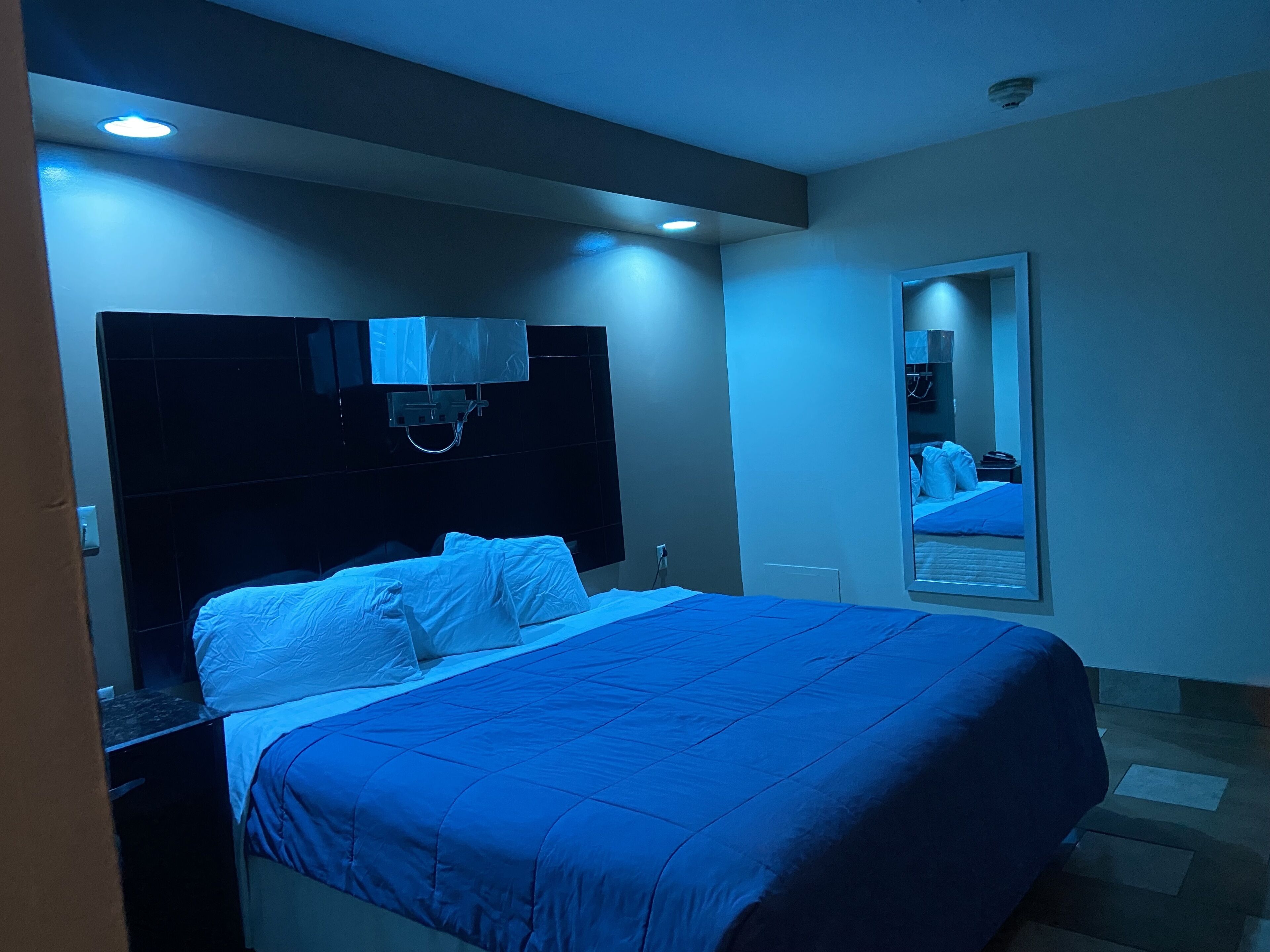Une chambre d’hôtel moderne avec un grand lit, une tête de lit intégrant un téléviseur et un miroir au mur.