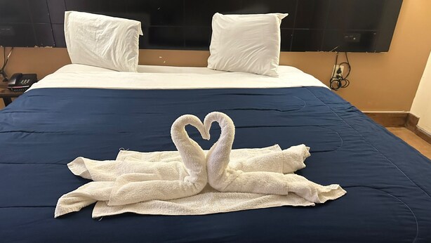 A hotel room with a bed, white pillows, and a towel arranged in a heart shape.