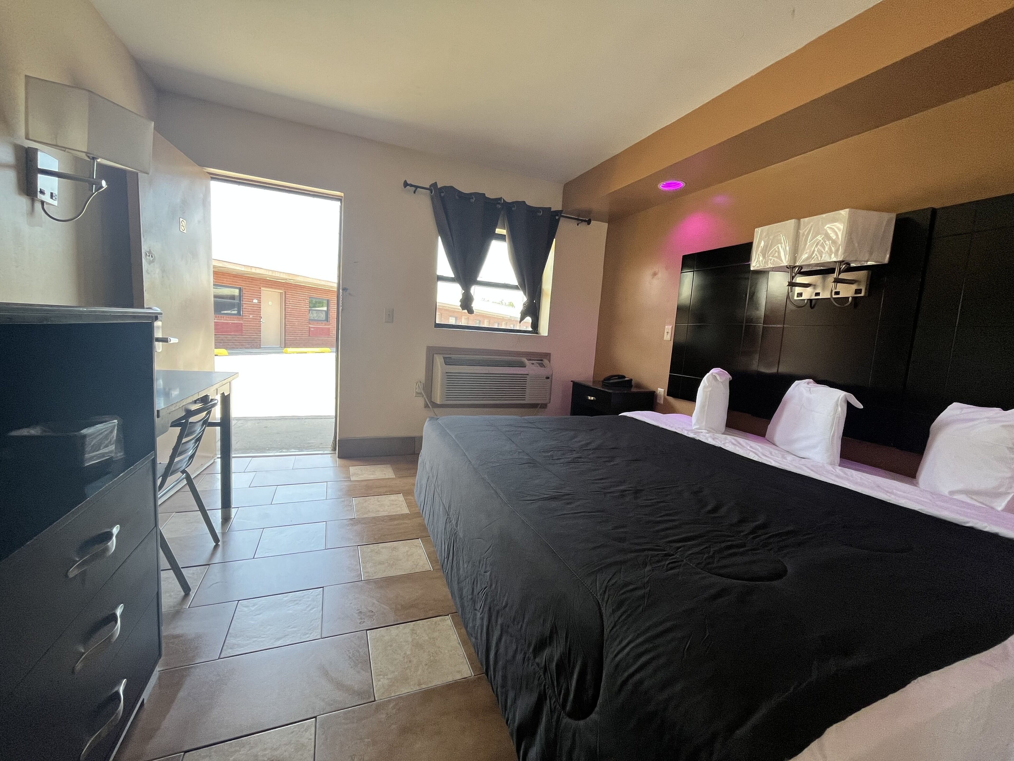 A hotel room with a bed, a desk, a dresser, and a window with curtains.