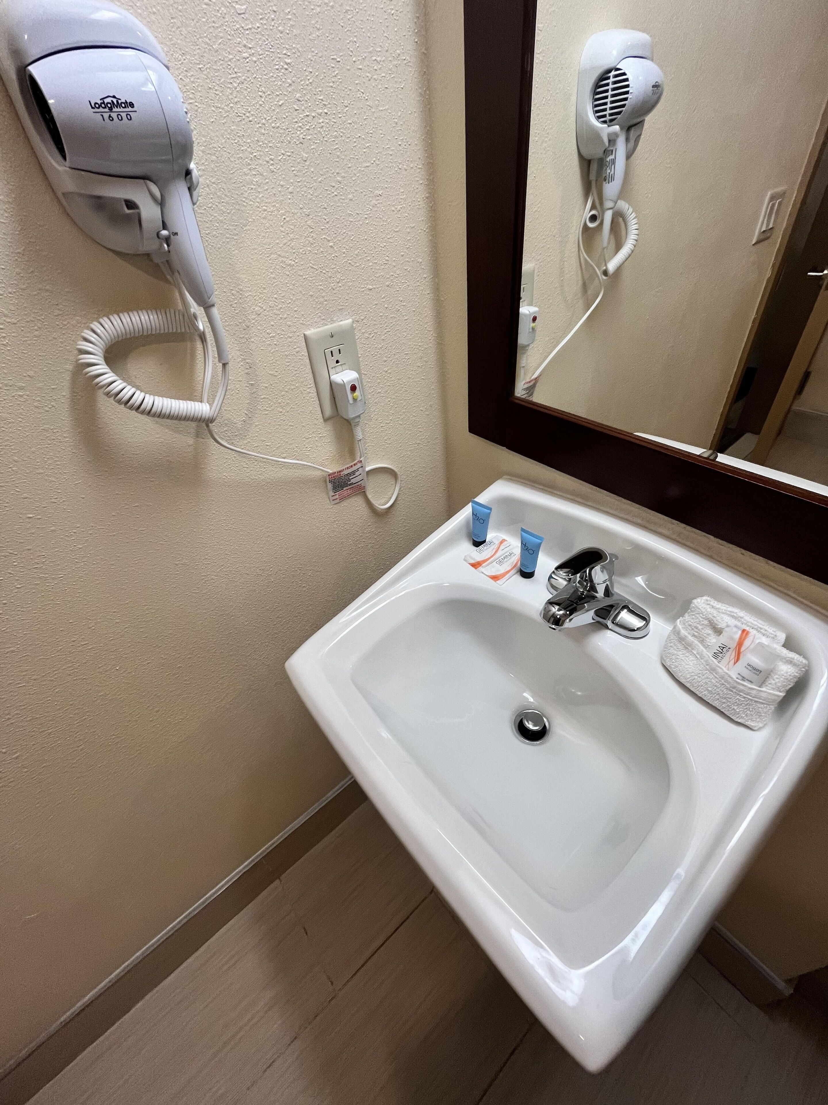 A bathroom with a white sink, a mirror, a hairdryer, and toiletries.