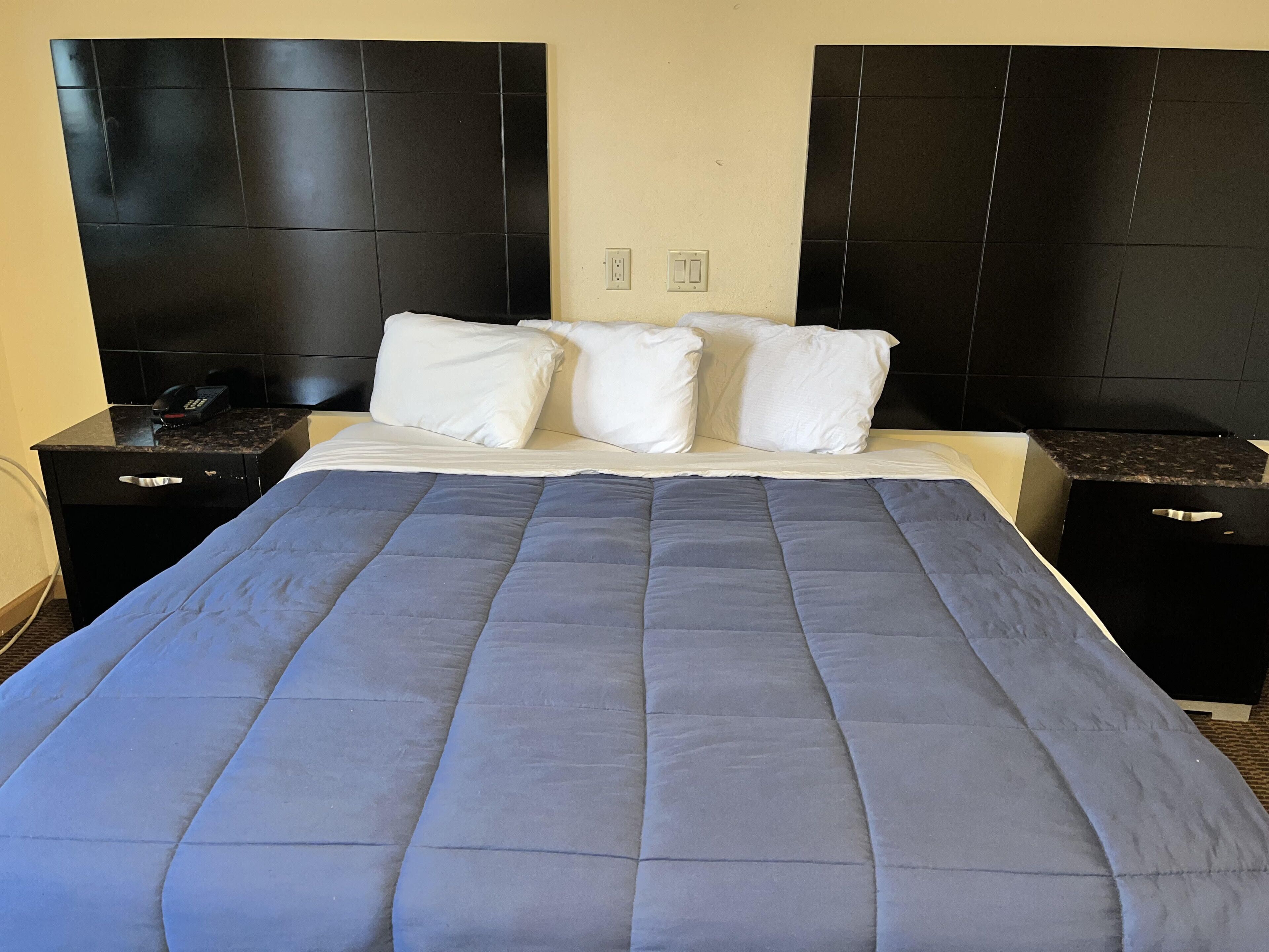 Ein Hotelzimmer mit einem großen Bett, einem schwarzen Kopfteil, weißen Kissen und einer blauen Bettdecke.