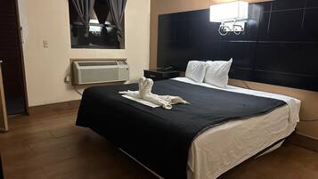 Une chambre d’hôtel avec un grand lit, une tête de lit dotée d’un luminaire, un appareil de climatisation et une fenêtre avec des rideaux.