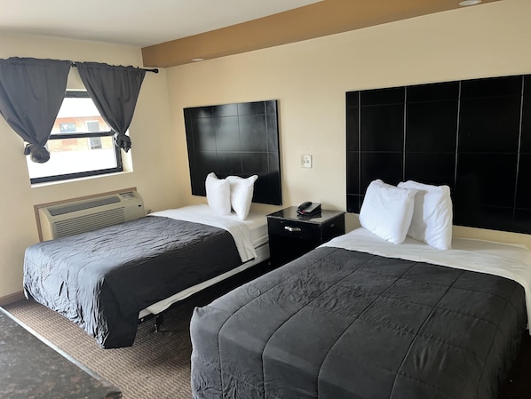Habitación de hotel con dos camas, cabecera negra, mesita de noche con teléfono y ventana con cortinas.