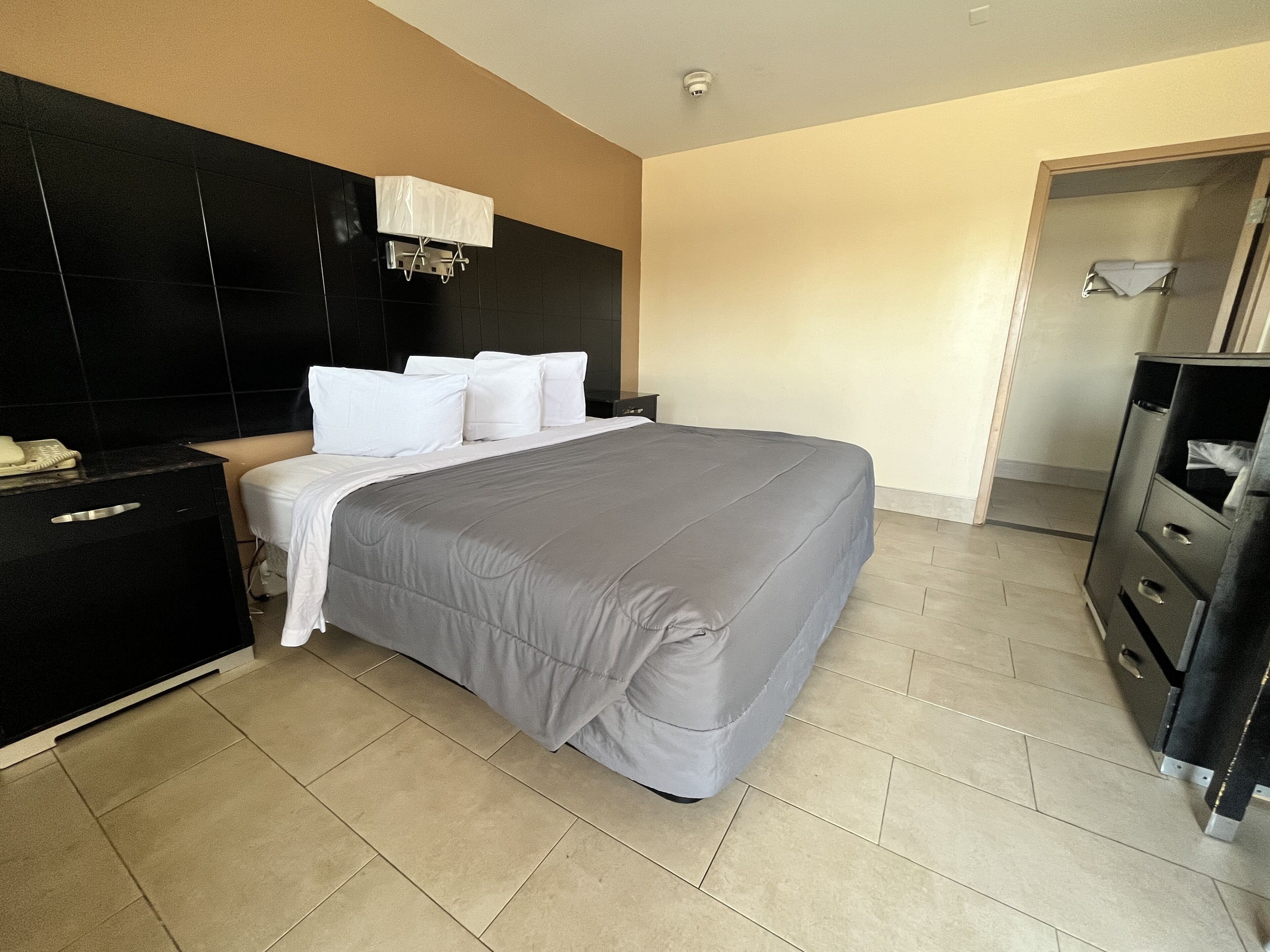 A hotel room with a large bed, a black headboard, a bedside table with a telephone, and a wardrobe.