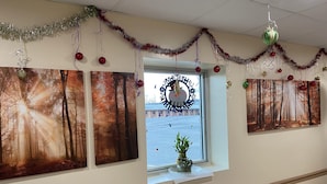 A hallway with three framed forest scenes, a window with a wreath, and festive decorations.