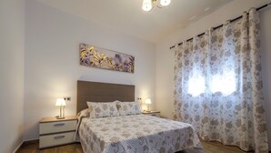 A bedroom with a bed, two bedside tables, a nightstand, a wall-mounted lamp, and a window with curtains. - Chalet Conil Ramirez with private pool (Conil de la Frontera)