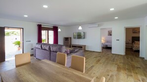 A modern living room with a wooden dining table, a grey sofa, and a TV mounted on the wall. - Chalet Conil Ramirez with private pool (Conil de la Frontera)
