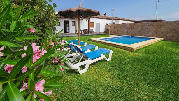 A pool area with two sun loungers, a small building with a thatched roof, and a stone wall. - Chalet Conil Ramirez with private pool (Conil de la Frontera)