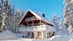 A wooden chalet with a balcony, surrounded by snow-covered trees. - Kulma-alpit b by Interhome (Hyrynsalmi)