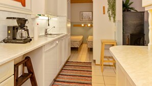 A compact kitchen with white cabinets, a coffee maker, and a sink. There is a small wooden table and a chair in the dining area. - Kulma-alpit b by Interhome (Hyrynsalmi)
