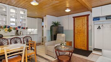 Un interior acogedor con comedor, sala de estar con sofá y sillón, cocina con armarios blancos y una puerta de madera.