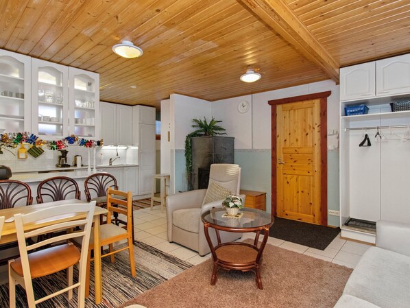 Un interior acogedor con comedor, sala de estar con sofá y sillón, cocina con armarios blancos y una puerta de madera.