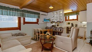 A cozy living room with a sofa, armchair, and a small table with chairs. There is a kitchen area with cabinets and a window. - Kulma-alpit b by Interhome (Hyrynsalmi)