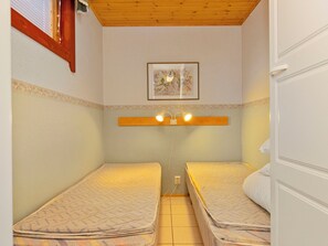 Una habitación pequeña y funcional con dos camas individuales, techo de madera, un cuadro enmarcado en la pared y una puerta blanca.