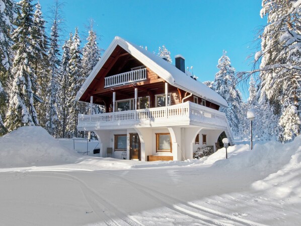 Een houten chalet met twee verdiepingen en een balkon, omgeven door met sneeuw bedekte bomen.