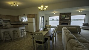 A spacious kitchen with a dining area, a fireplace, and a large window overlooking a body of water. - Waterfront property 25 min from Waterton (Hill Spring)
