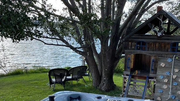 A hot tub with a wooden deck, a tree, and a rock climbing wall. - Waterfront property 25 min from Waterton (Hill Spring)