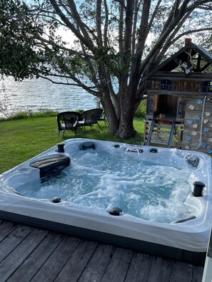 A hot tub with a wooden deck, a tree, and a rock climbing wall.
